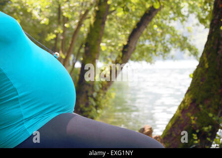 Closeup of tummy of a pregnant woman relaxing in the nature near a lake in a wood Stock Photo