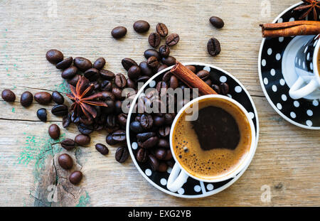 Black and white dots cup of coffee on the old wooden table with coffee beans, cinnamon sticks and anise star Stock Photo