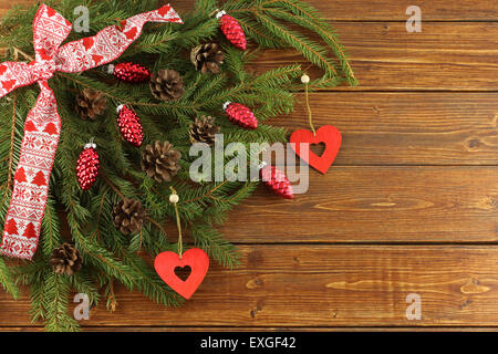 Christmas Wreath - red cones and red wooden hearts on green spruce branches on brown wooden background Stock Photo