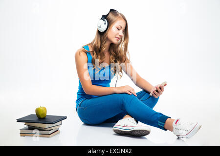 Beautiful young woman sitting on the floor with headphones and using smartphone isolated on a white background Stock Photo