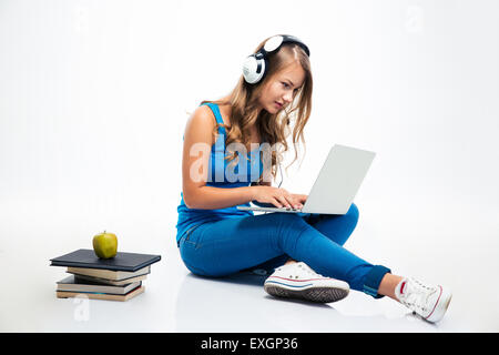 Beautiful young woman sitting on the floor with headphones and using laptop isolated on a white background Stock Photo