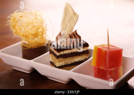 Three beautiful delicious gourmet desserts on a white plate. Chocolate layered cake, fudge, mousse and turkish delights. Stock Photo