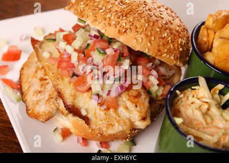 Delicious chicken burger with chopped salad served with potato wedges on a white plate on a wooden table. Stock Photo