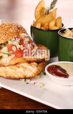 Delicious chicken burger with chopped salad served with potato wedges on a white plate on a wooden table. Stock Photo