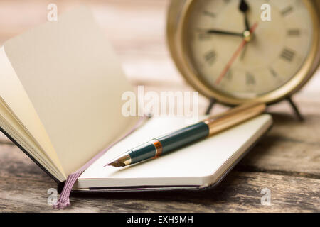 Open small notebook with fountain pen and old-fashioned alarm clock behind. Writing background image with selective focus Stock Photo