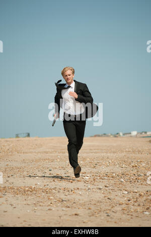 man holding a gun and running a long the beach in a black suit Stock Photo