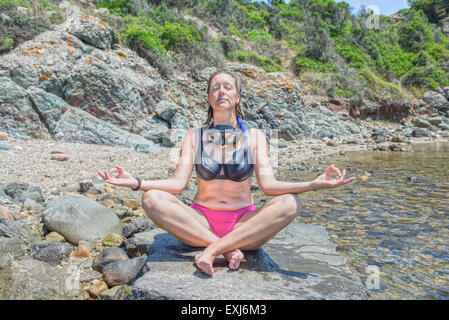 Woman sat on a rock on a beach meditating Stock Photo