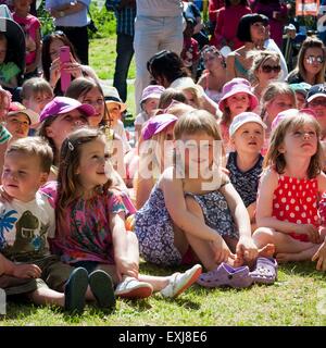 Audience of children sat on the grass in the sunshine watching a Punch and Judy show Stock Photo