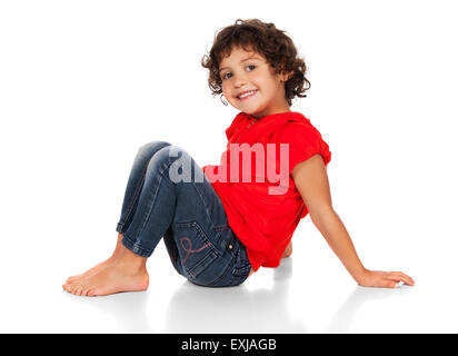 Adorable small caucasian child with curly hair wearing a bright red hooded top and blue jeans. The girl is sitting and smiling a Stock Photo