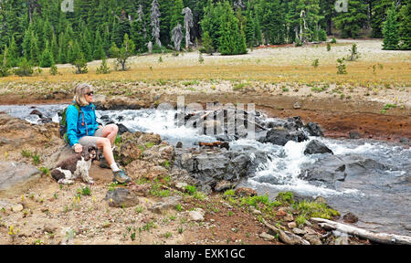 A hiker and her cocker spaniel sit beside a mountain stream in the Oregon Cascade Mountains near Broken top Peak. Stock Photo