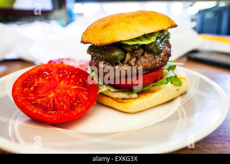 A Hamburger on a Torta roll with a fresh homegrown tomato from the garden with pickle and Romaine lettuce on a desk for lunch Stock Photo