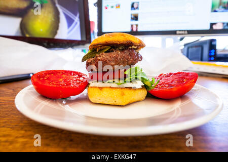 A Hamburger on a Torta roll with a fresh homegrown tomato from the garden with pickle and Romaine lettuce on a desk for lunch Stock Photo