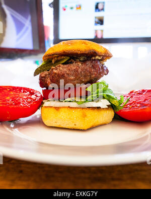 A Hamburger on a Torta roll with a fresh homegrown tomato from the garden with pickle and Romaine lettuce on a desk for lunch Stock Photo