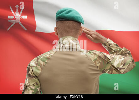Dark-skinned soldier in hat facing national flag series - Oman Stock Photo