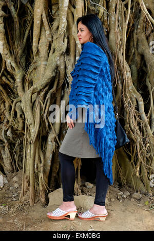 pretty well dressed local female posing in front of tree with large roots in a park in the center of malang java indonesia Stock Photo