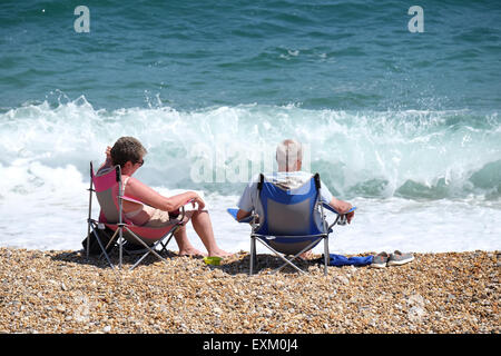 Torcross, Devon, UK. Two people sat in beach chairs at water's edge on shingle beach at Torcross in Devon. Stock Photo