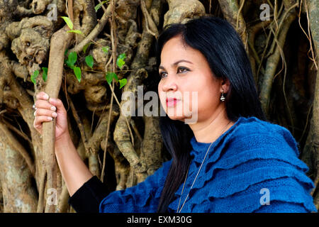 pretty well dressed local female posing in front of tree with large roots in a park in the center of malang java indonesia Stock Photo