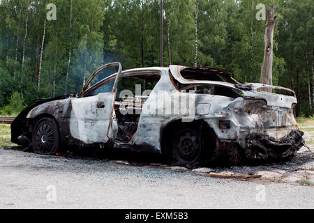 Burnt out rusted old car near the road and forest Stock Photo