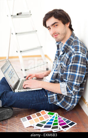 View of a Young man using laptop while choosing color of his flat Stock Photo