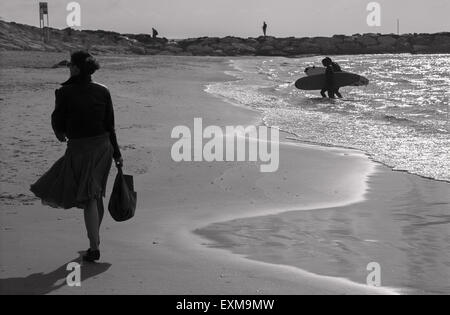 TEL AVIV, ISRAEL - MARCH 2, 2015: The silhouette of walked woman and surfers on the beach of Tel Aviv. Stock Photo