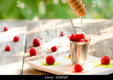 Raspberries in a steel cup with flowing honey from a dipper on vintage wood background Stock Photo