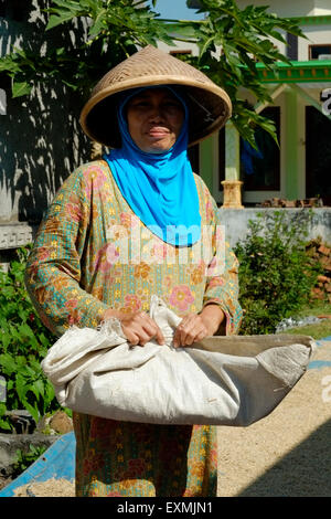 local female preparing rice spread out to dry in the sunshine in a rural village in java indonesia Stock Photo