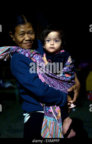 elderly lady acting as a nanny carrying baby girl in a sarong in the early hours of the morning in java indonesia Stock Photo