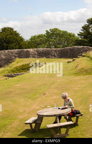 Woman sitting looking at guidebook about the Iron Age hill fort hillfort at Old Sarum, near Salisbury, Wiltshire UK in July Stock Photo