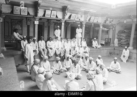 Villagers of munagoli dressed in traditional white turbans or white caps gather in courtyard of old house of landlord Stock Photo