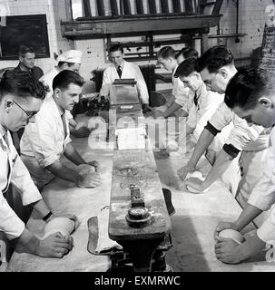1950s historical picture showing a group of male students or apprentices at long tables being taught how to prepare and shape the dough for bread making. Stock Photo