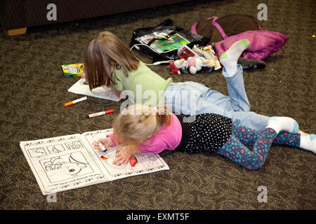 Two young girls concentrating on drawing in coloring books on floor. St Paul Minnesota MN USA Stock Photo