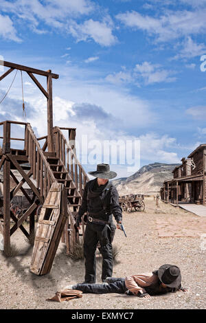 Two cowboys in the street, one on the ground and the other holding a gun on him, gallows in the background, Old Trail Town, Cody Stock Photo