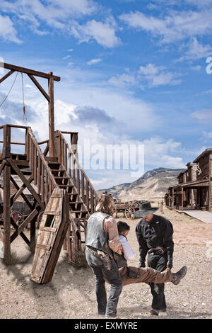 Two men carry a third man, wounded, away from the Gallows at Old Trail Town, Cody, Wyoming. Stock Photo