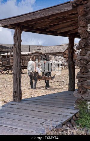 Two men carry a third man, wounded, down the street in Old Trail Town, Cody, Wyoming. Stock Photo