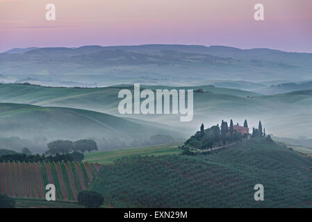 Foggy sunrise with a pink sky and mist between the Tuscan hills over agriturismo podere il Belvedere farmhouse in the Valdorcia. Stock Photo