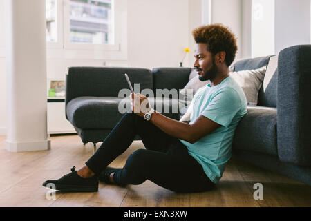Young man at home reading messages on smart phone Stock Photo