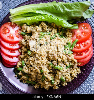 A plate of couscous with basil and spices served with tomato slices and lettuce leafs on a purple transparent plate Stock Photo