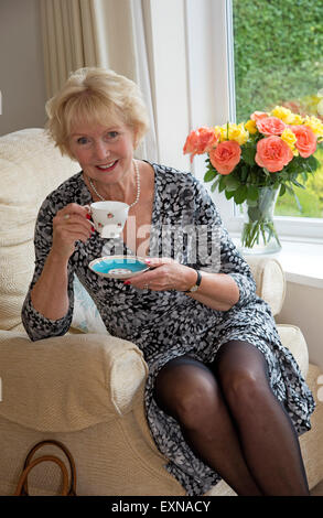 Elderly woman sitting in a comfortable chair having a cup of tea Stock Photo