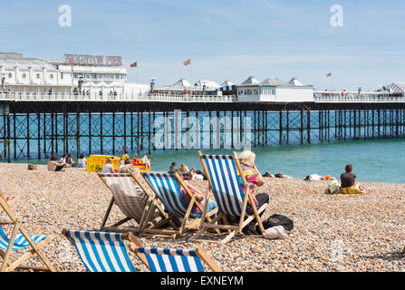 Holidaymakers relaxing on blue and white striped deckchairs on Brighton beach by the pier on a hot, sunny summer day, Brighton, East Sussex, UK Stock Photo