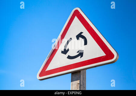 Traffic roundabout, triangle road sign over blue sky background Stock Photo