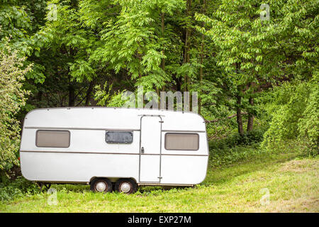 Old camping trailer standing in woods on summer day, nature holiday concept. Stock Photo