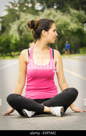 Hispanic brunette in yoga clothing sitting with legs crossed and arms down touching ground while looking to the side Stock Photo
