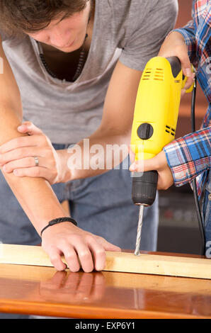 Closeup of couple working together as man holding wooden piece down on table while woman using power drill Stock Photo