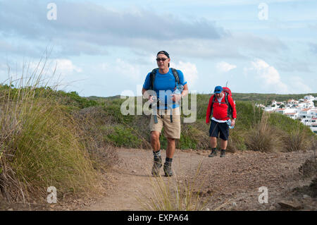 Two walkers leave Es Grau village on the Cami de Cavalls bridal path on the island of Menorca Spain Stock Photo