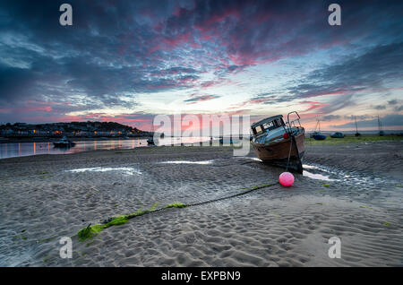An old wooden boat under a fiery dusk sky on the beach at Instow near Bideford in Devon, looking out to Appledore Stock Photo