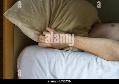 Young man on the bed with a cushion over his head Stock Photo