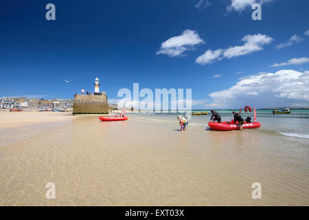 St Ives, Cornwall, UK: Family getting out of a red self-drive hire boat in the shallow water of the harbour beach on sunny day. Stock Photo