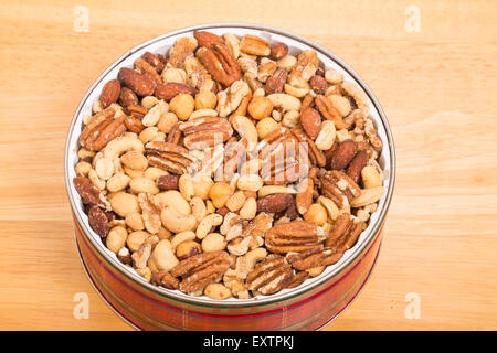A mixture of salty, roasted deluxe nuts in a red plaid tin on wood table Stock Photo