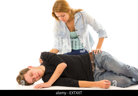 Couple demonstrating first aid techniques with male patient lying in recovery position and female sitting above him Stock Photo
