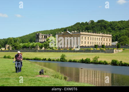 Two men walk on the banks of the River Derwent by Chatsworth House in the Peak District on a glorious summer day, Derbyshire UK